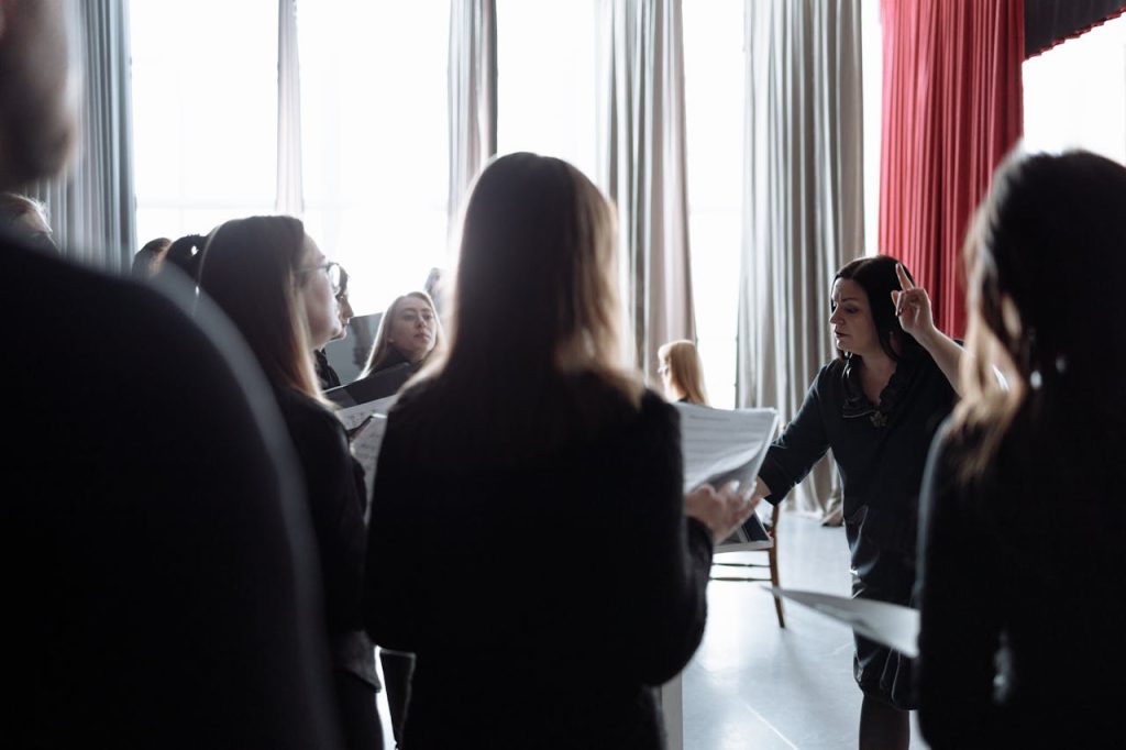 A choir group rehearsing indoors with a conductor guiding the performance.