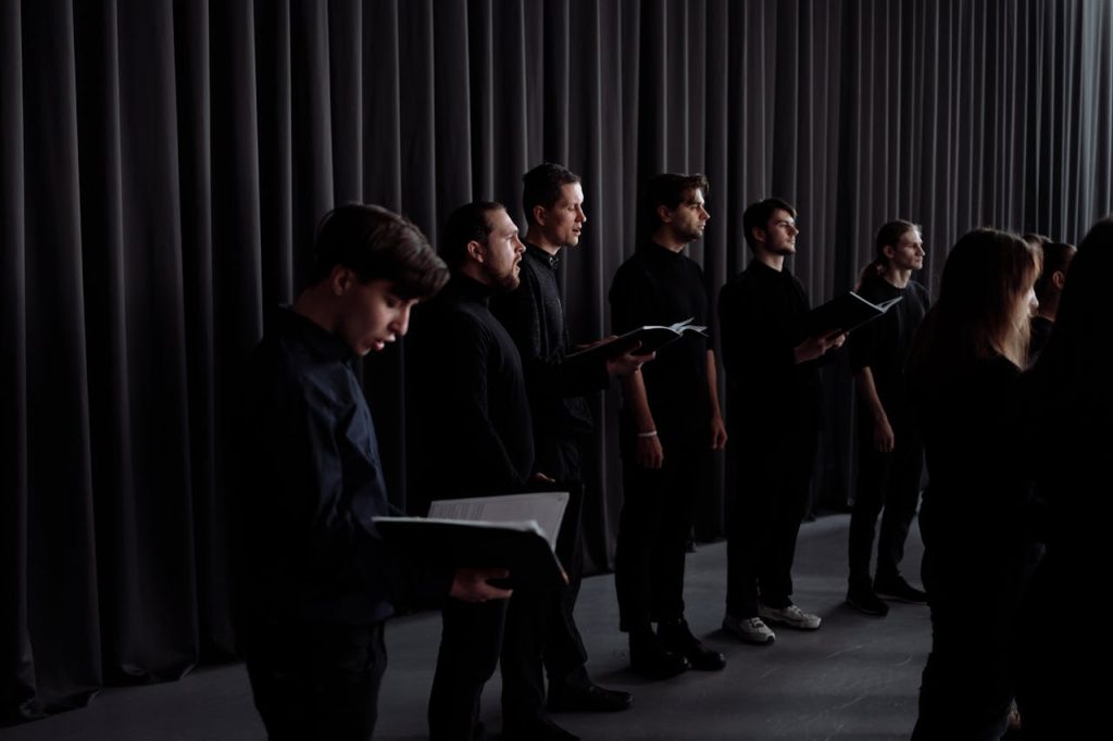 A choir group in black attire rehearsing indoors with music scores.